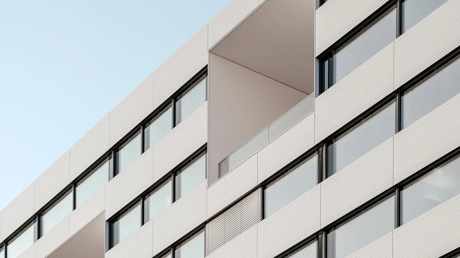 A modern residential building facade in pale panels with recessed balconies