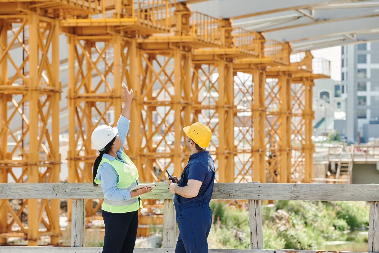 Two building professionals in hard hats on site, one pointing up at formwork, the kind of in-person inspection that automation must never replace