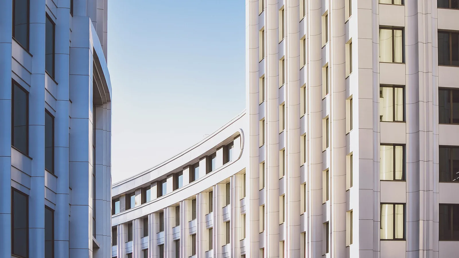 Curved white ribbed facades of two completed office buildings meeting against the sky