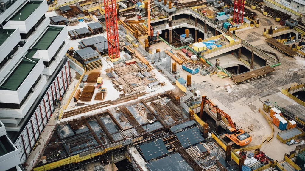 Aerial view looking down on a large multi-level city construction site with cranes, formwork and stacked materials