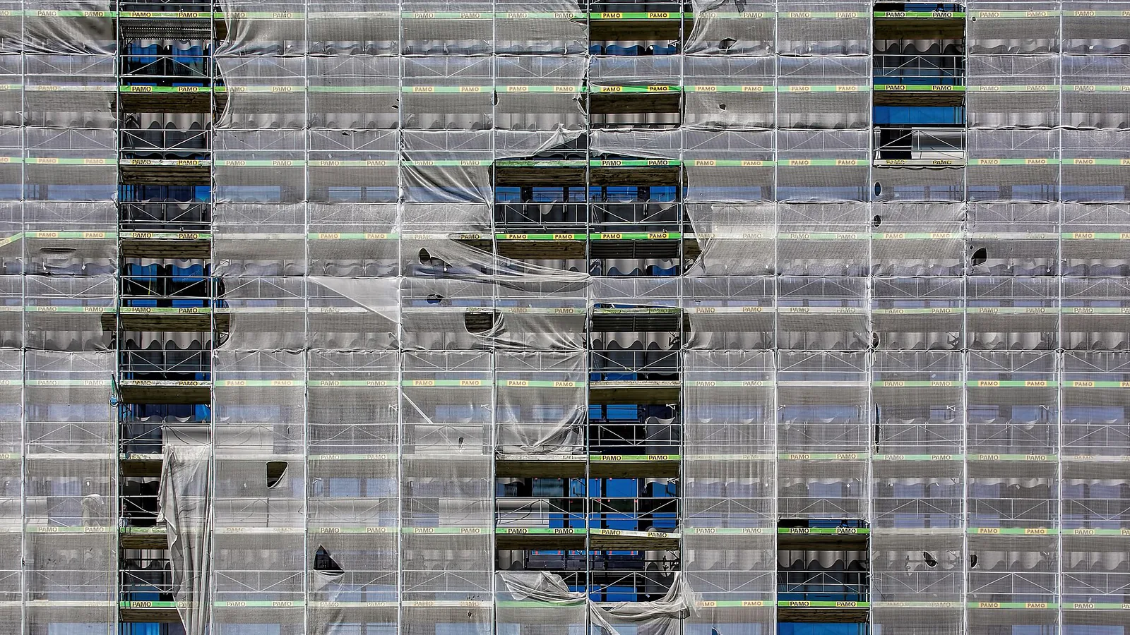 A tall building facade completely wrapped in scaffolding and protective mesh
