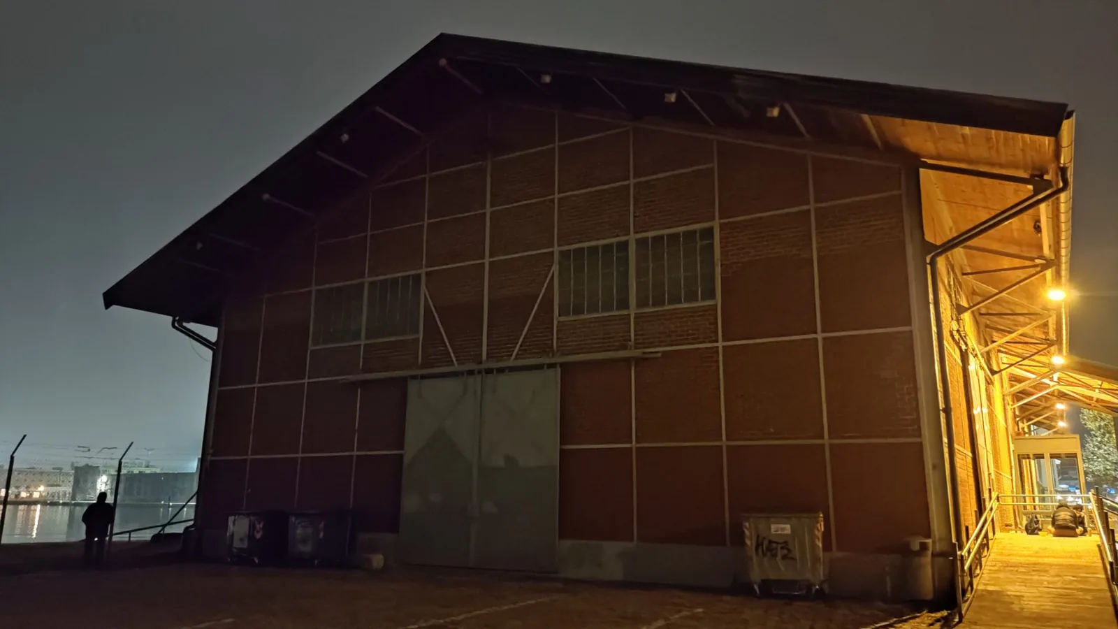 A large warehouse building at dusk with its loading door open and interior lights on