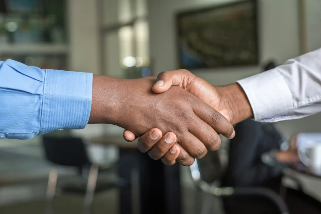 Two people shaking hands across a desk in an office, representing the named reviewer accountable for a human in the loop decision