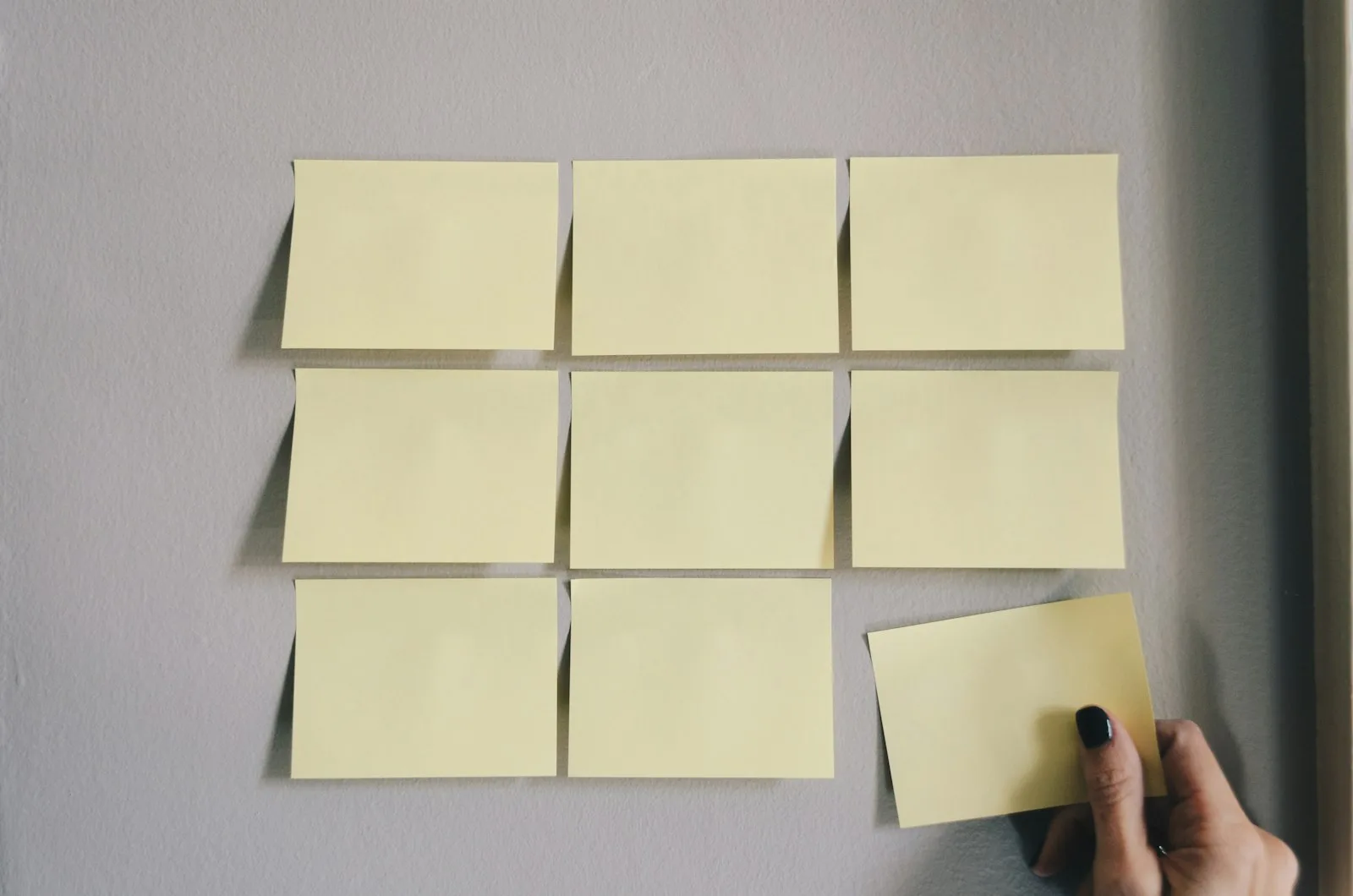 Nine blank yellow sticky notes arranged on a wall with a hand placing another, representing an audit trail of review decisions