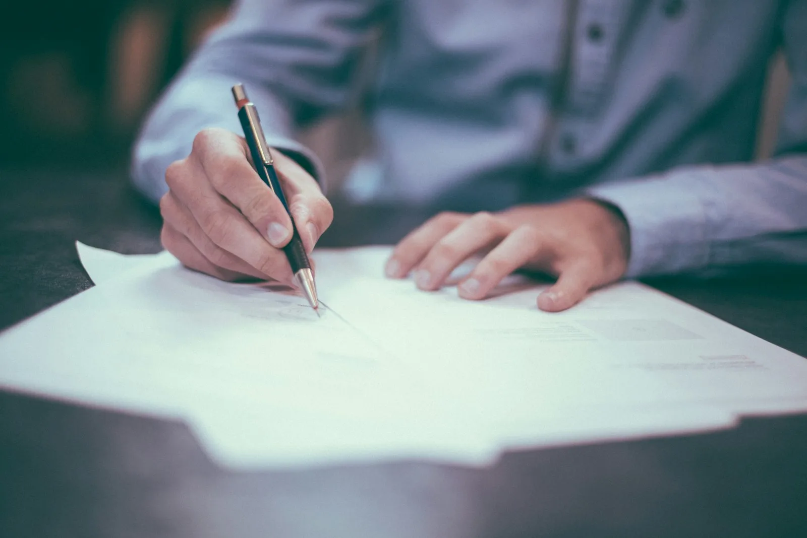 A person writing on paper with a pen at a desk, representing the timestamped record of a human review decision