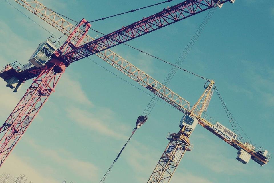 Two tower cranes silhouetted against a clear teal sky above a construction site