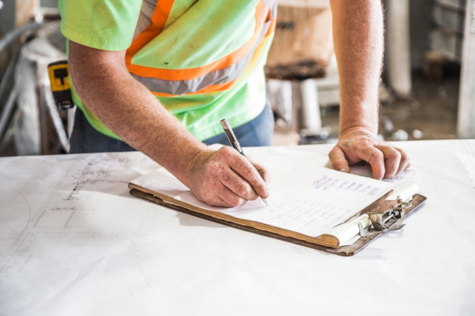 Worker in a high-visibility vest filling in a paper form by hand on a clipboard, an example of manual data entry in an Australian business