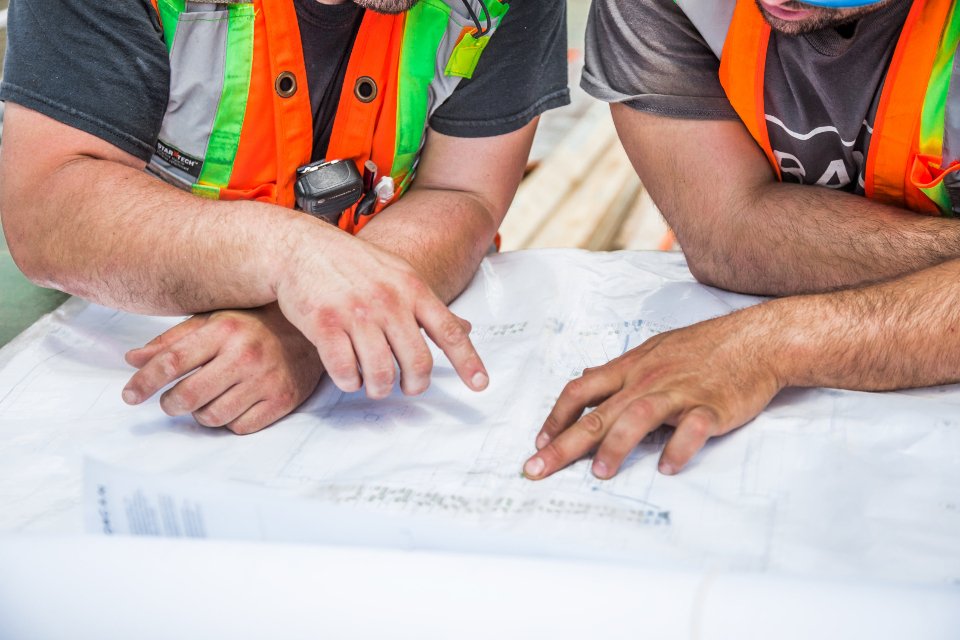 Two construction workers in hi-vis vests reviewing marked-up building plans on site