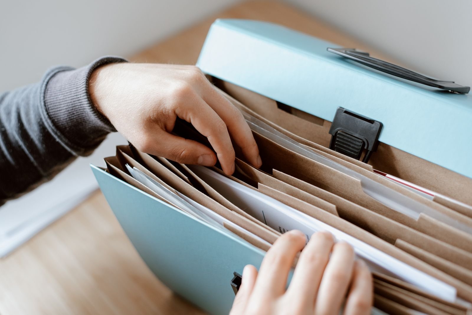 Hands flicking through the tabbed sections of a paper concertina file, the client filing that accounting compliance automation turns into a searchable register