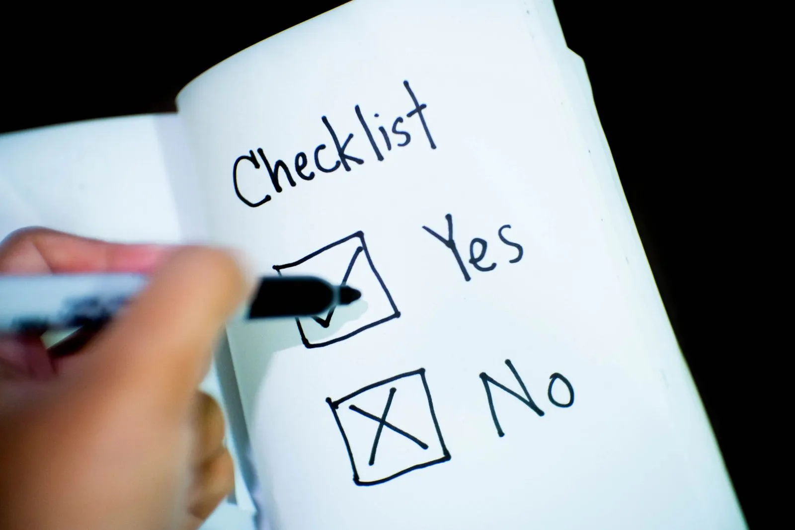 A hand ticks the Yes box on a printed checklist with a black marker: an ADM checklist in progress