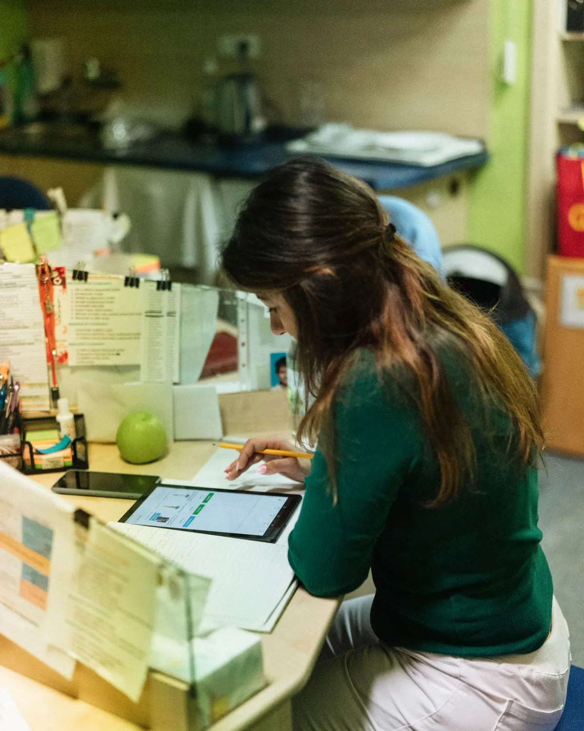 Nurse at a care facility desk reviewing records on a tablet beside printed folders, the document work AI automation for aged care handles