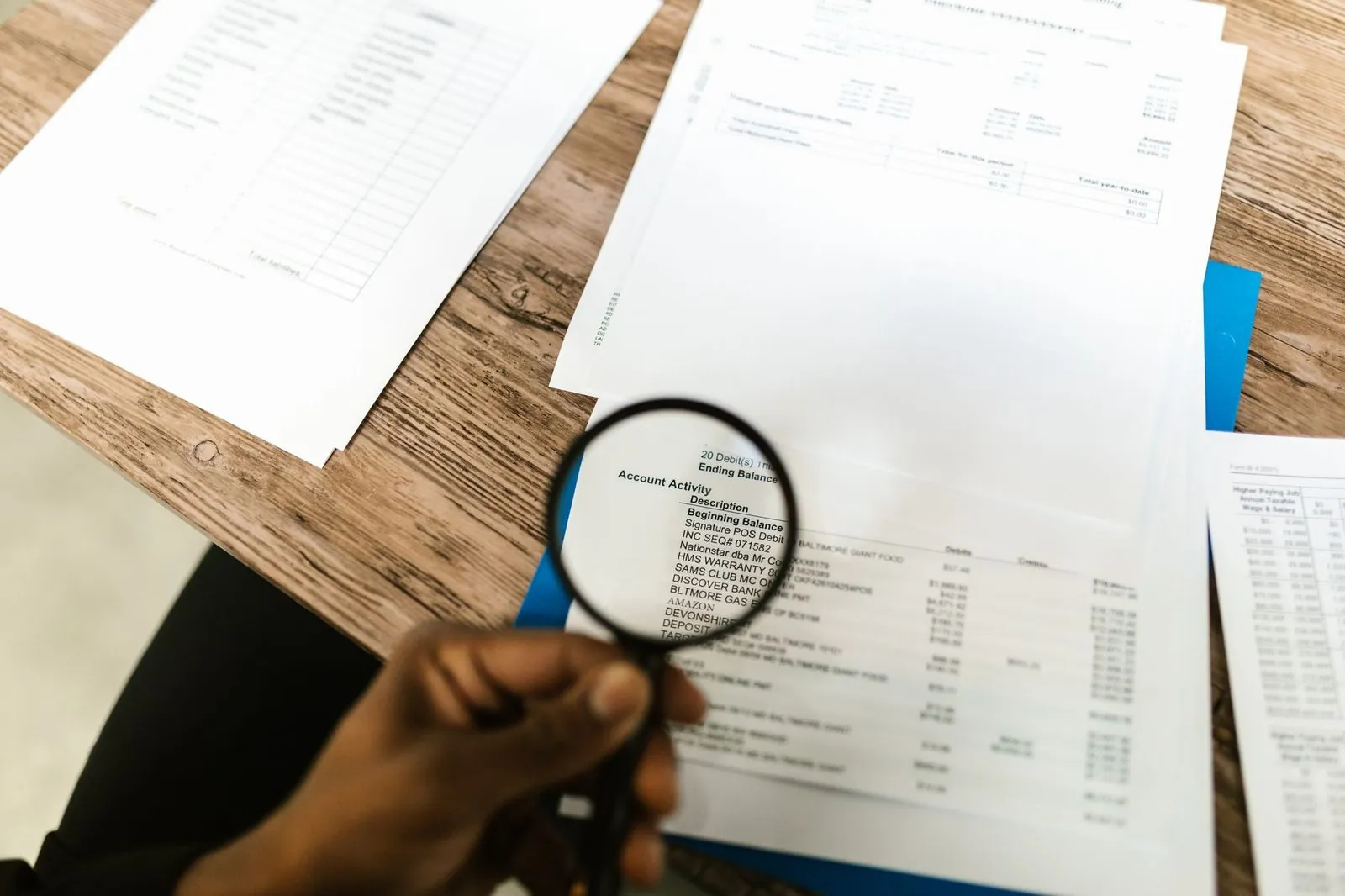 A hand holding a magnifying glass over a printed document on a wooden desk