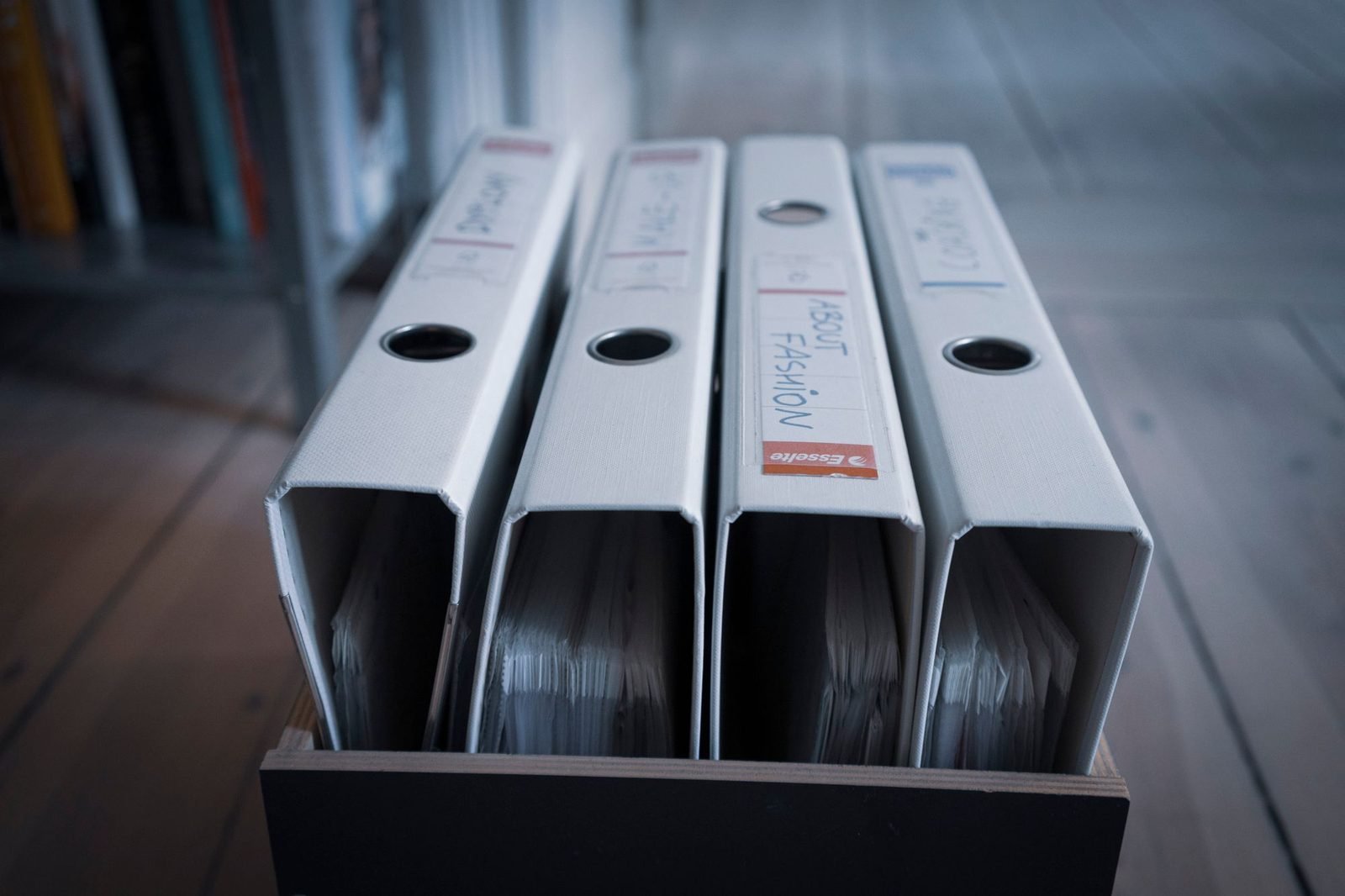 Several white ring binders standing upright in a cardboard archive box