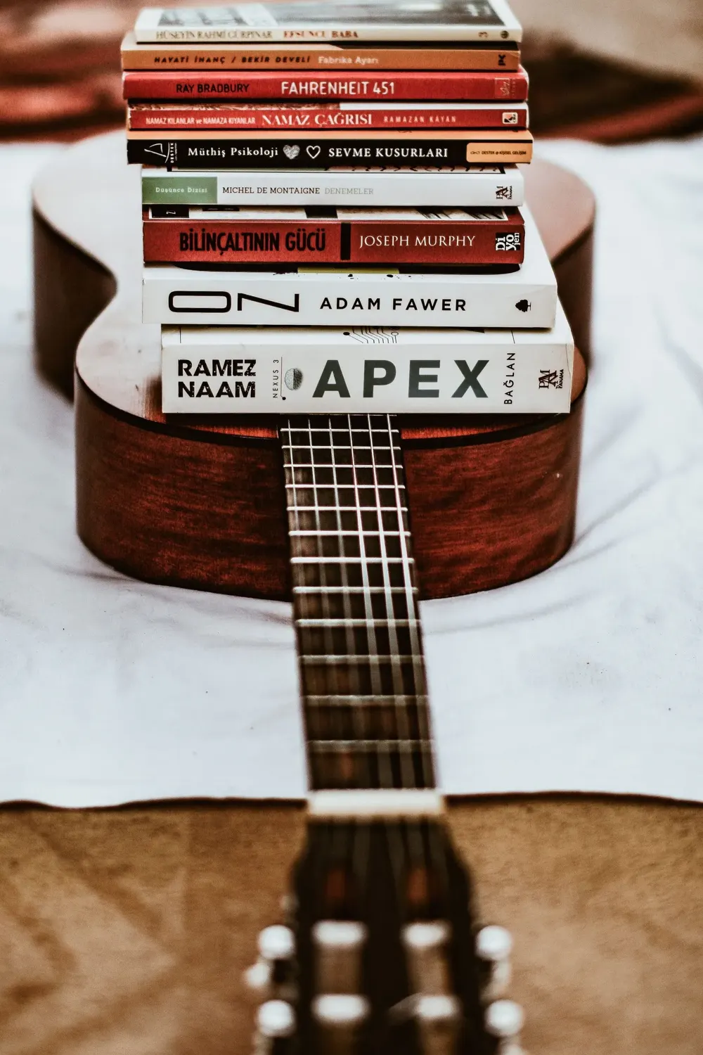 A stack of hardback books resting on the body of an acoustic guitar lying on a bed