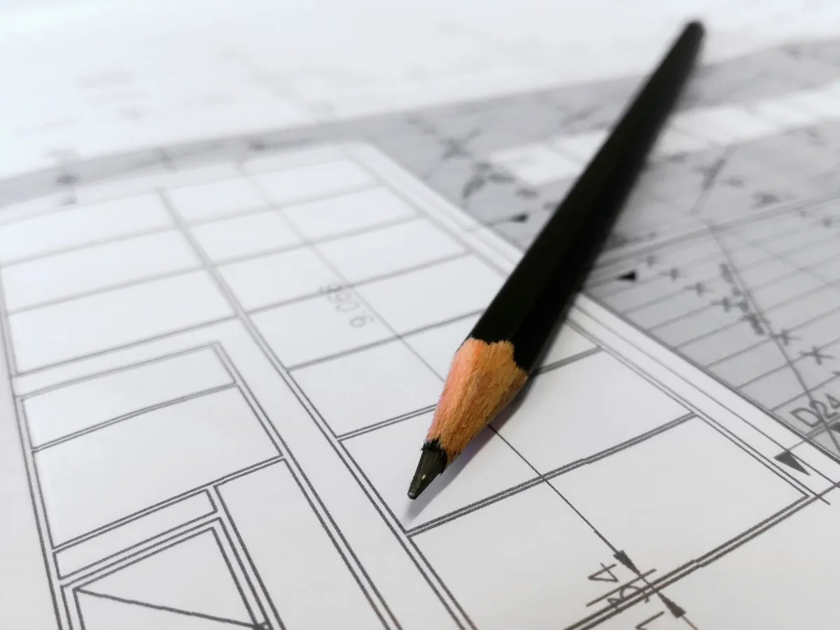 Architectural drawings and a pencil on a desk, the kind of plans building permit data extraction reads for lot numbers and title blocks