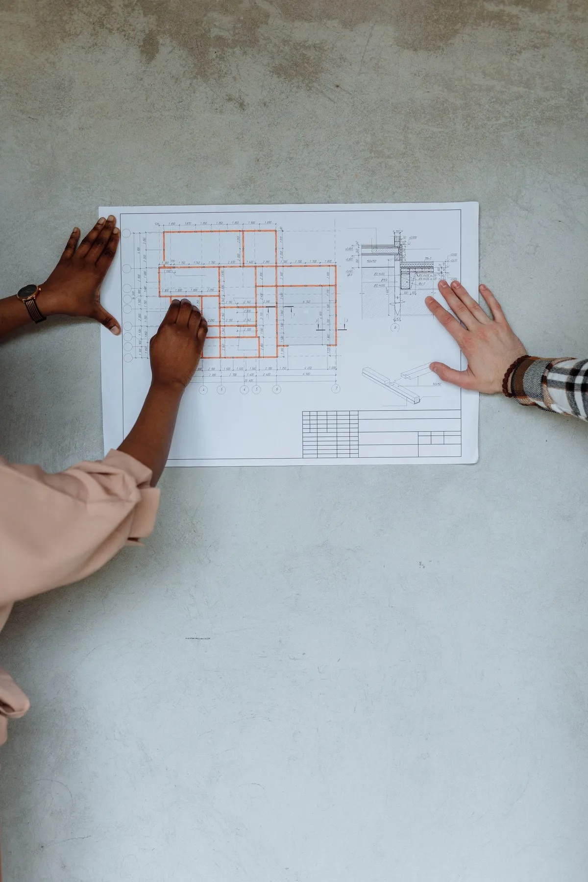 Two people holding a residential floor plan against a concrete wall while discussing a building permit