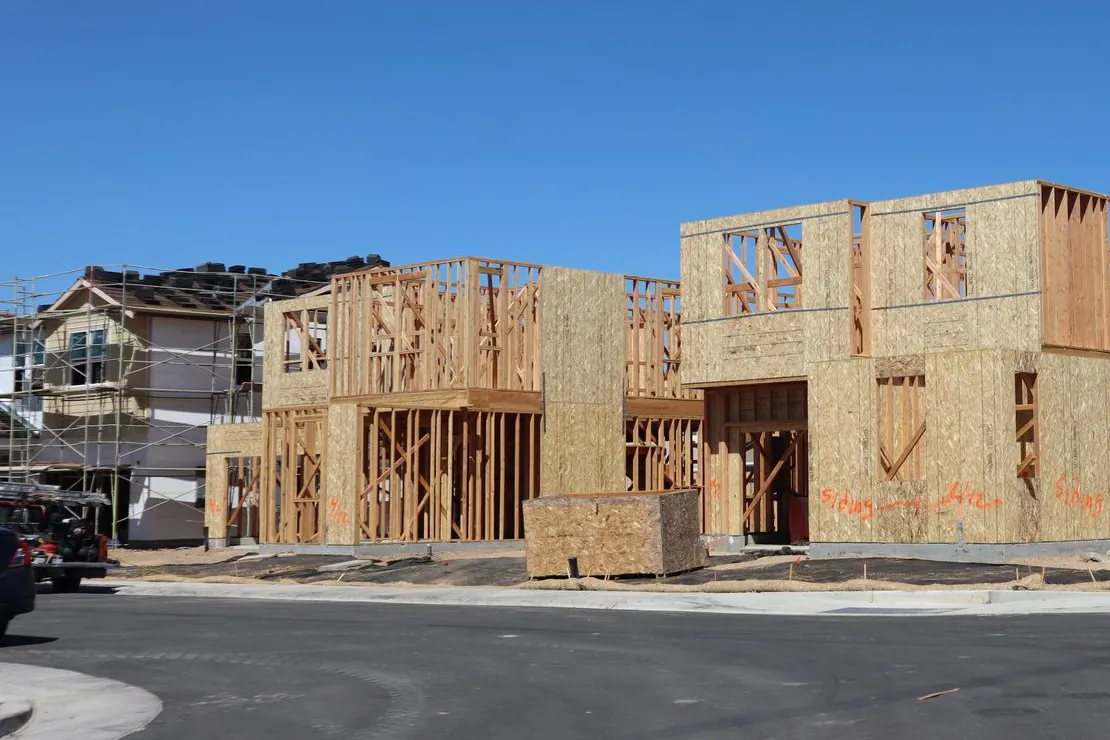 Timber house frames under construction beside scaffolding on a new residential estate, the frame stage that mandatory notification tracking follows