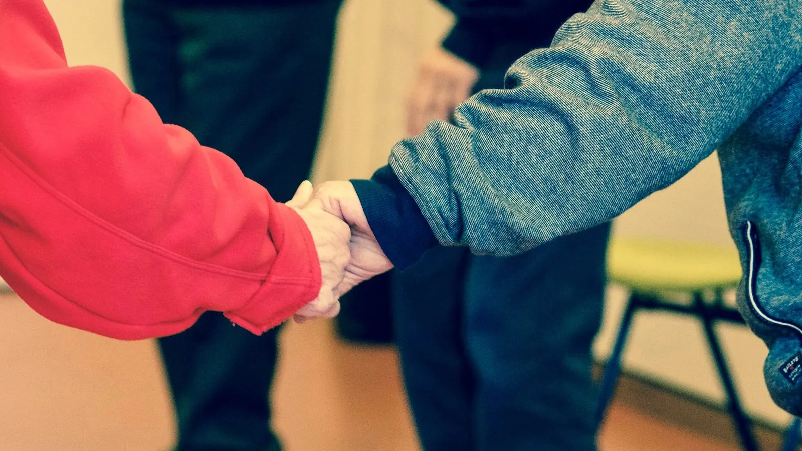Close up of a carer in a red top holding the hands of an older person in a grey jacket