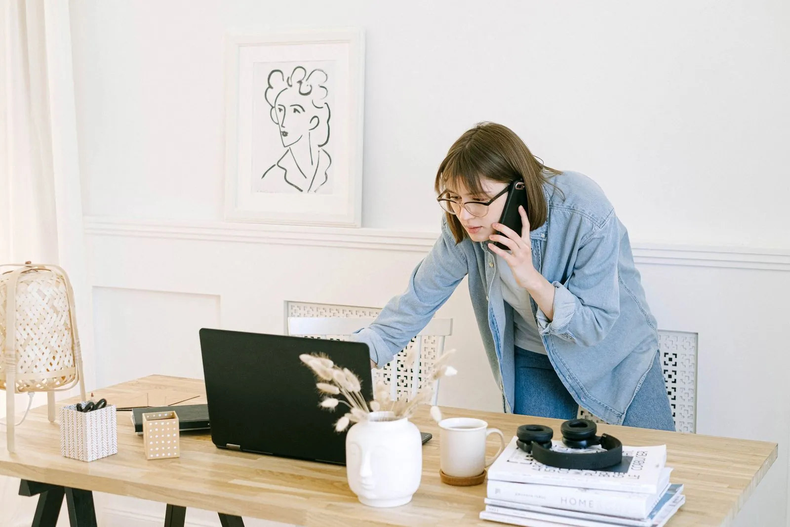 A consultant in a denim shirt on the phone, leaning over a laptop at a bright wooden desk
