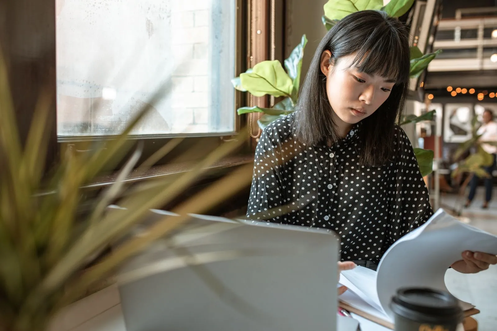 A consultant in a polka dot shirt reading through printed documents beside an open laptop