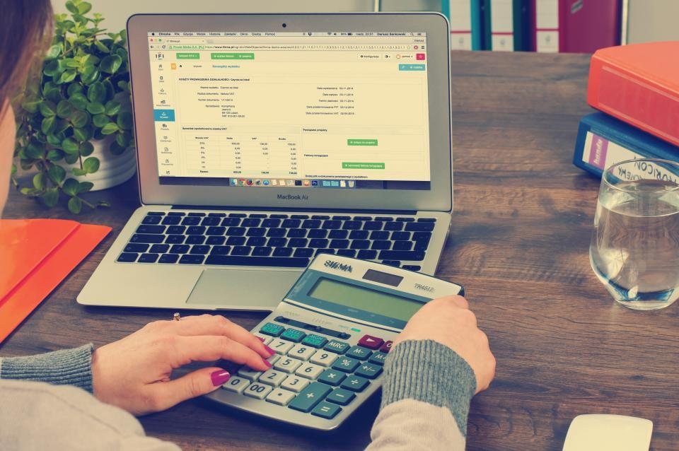 Hands using a calculator beside a laptop showing accounting software, keying supplier invoices by hand before you automate invoice processing in Xero
