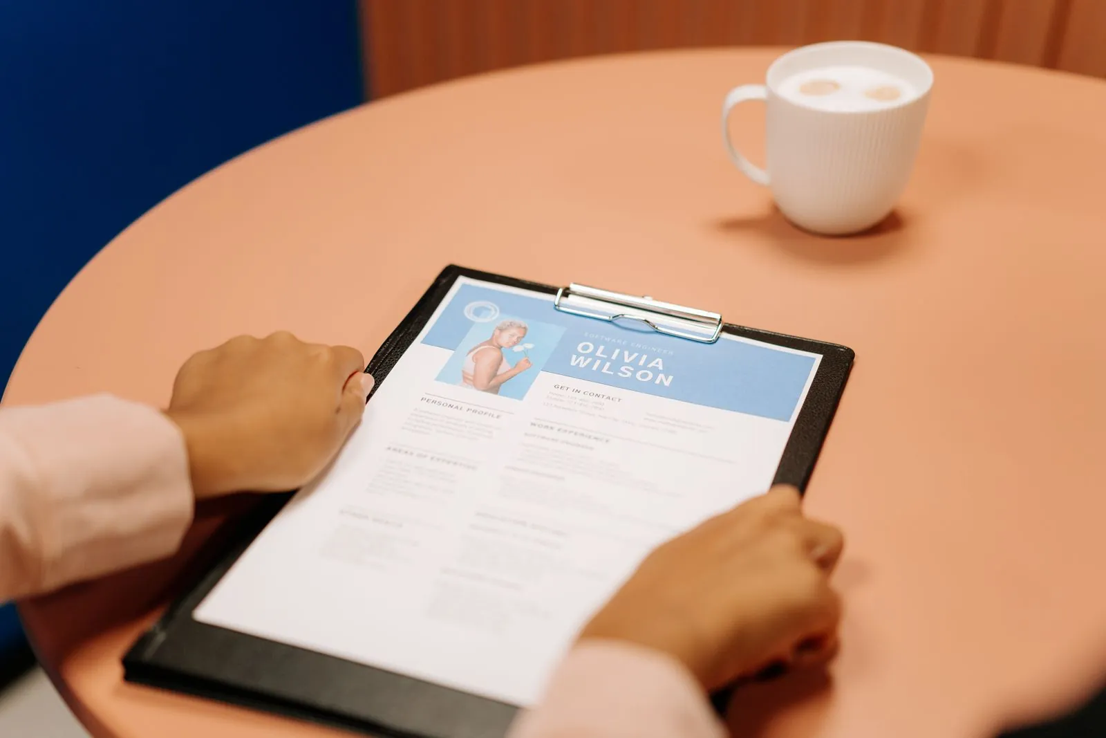 Hands holding a clean branded resume on a clipboard beside a coffee cup, the end result of CV reformatting
