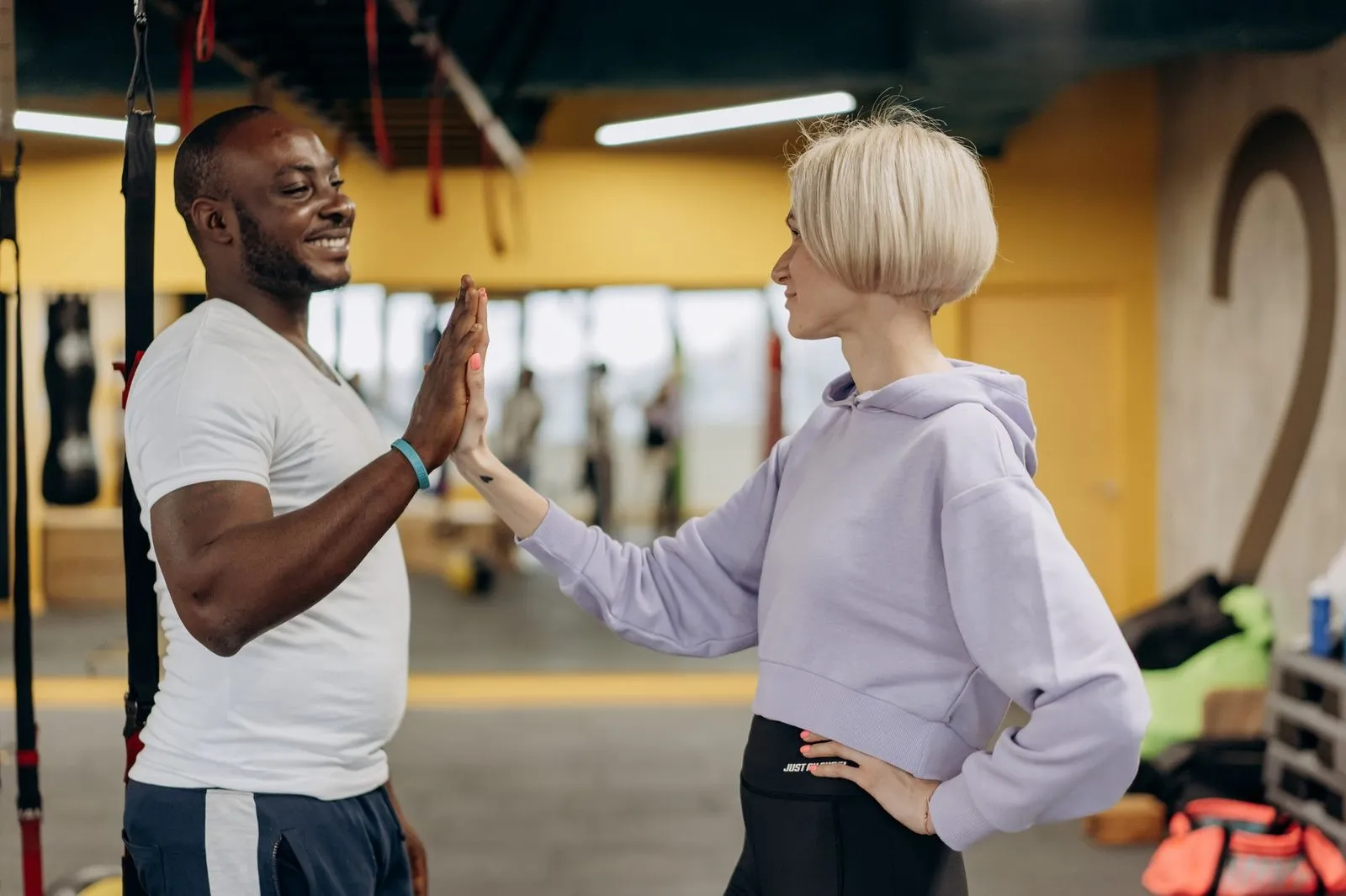 A man and a woman in workout clothes share a high five in a colourful gym