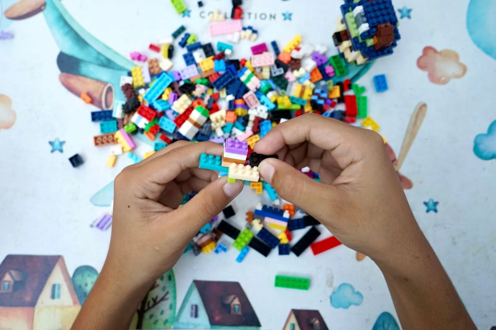 Two hands press small multicoloured plastic bricks together above a heap of loose bricks on a children's play mat