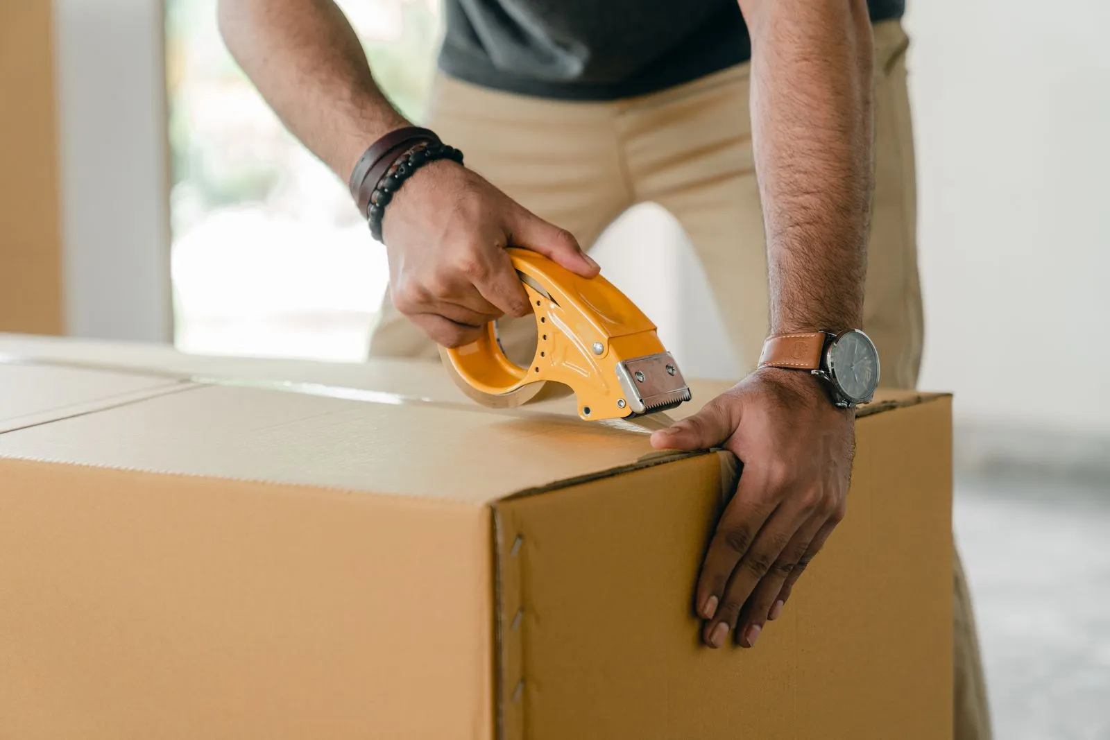 Close up of hands sealing a cardboard box with a yellow tape dispenser