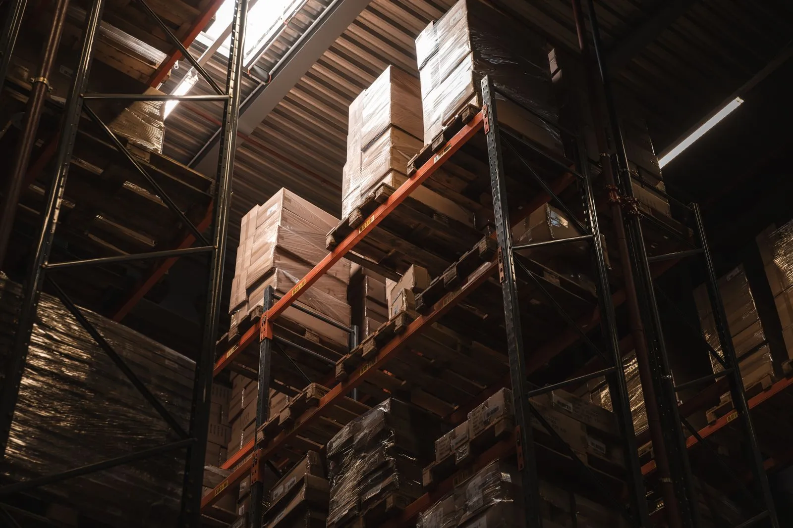 Tall warehouse racking stacked with cardboard boxes in warm light, the stock that inventory reorder automation keeps an eye on