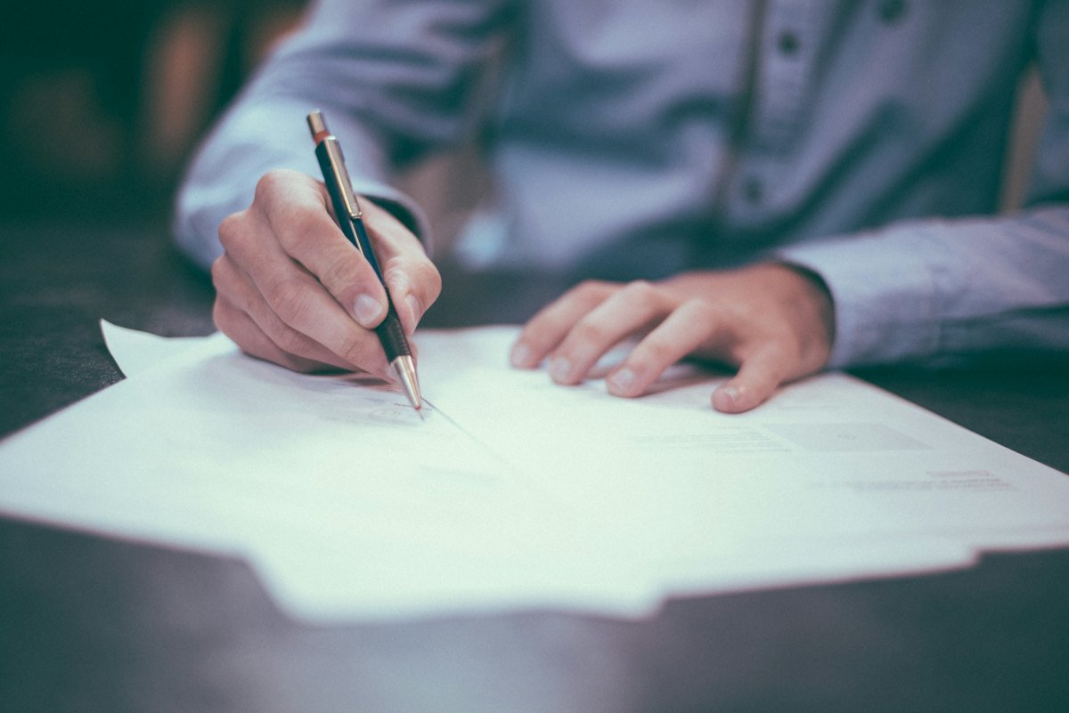 A person filling in a paper form by hand at a desk, representing the 21 minutes of handling in a manual invoice process