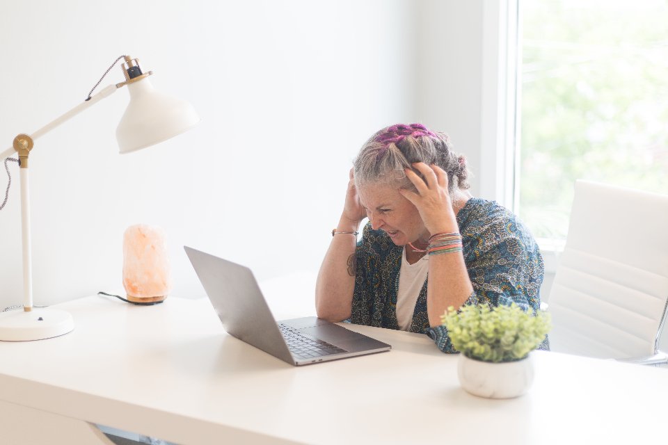 A woman at a desk with her head in her hands in front of a laptop, the Monday feeling of building a manual Excel report