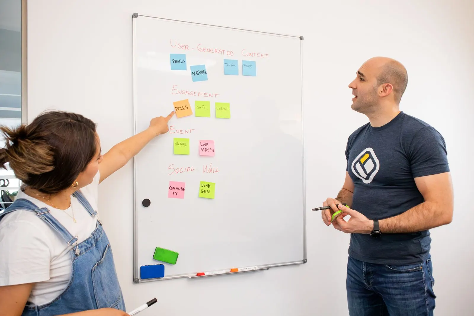 Two colleagues map a business process on a whiteboard covered in colourful sticky notes