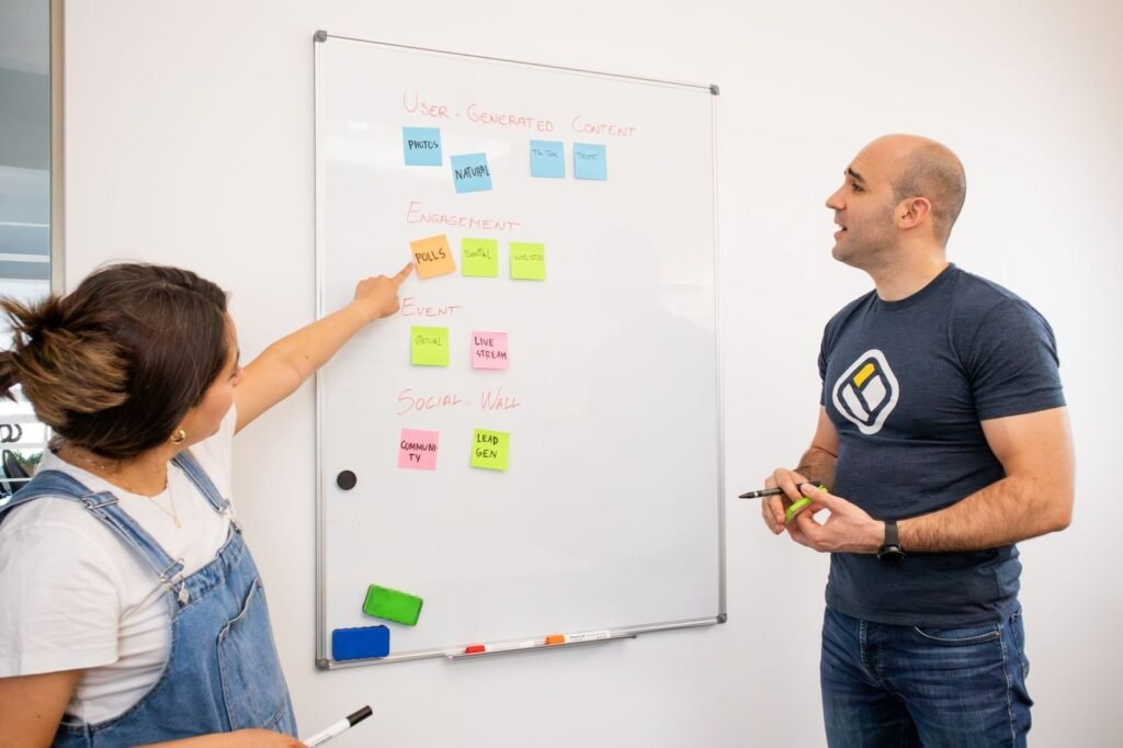 Two colleagues mapping a workflow with sticky notes on a whiteboard