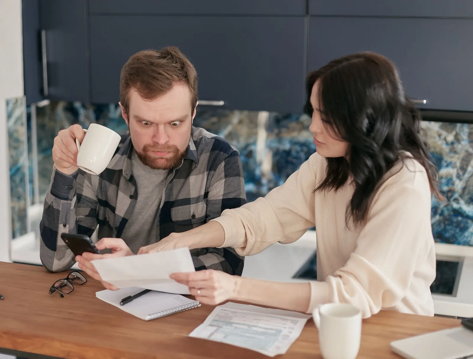 A man holding a coffee mug stares wide-eyed at a printed AI consulting quote while his partner reads the figures beside him