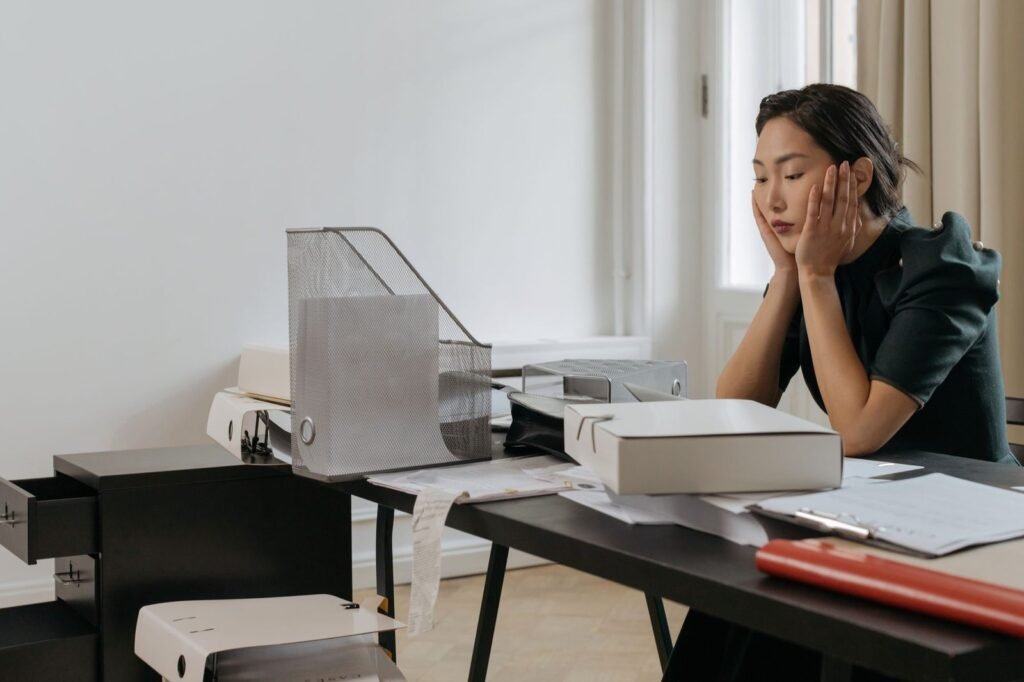 An office manager with her head in her hands beside a desk of folders and trays, the paperwork regulated document intelligence is built for