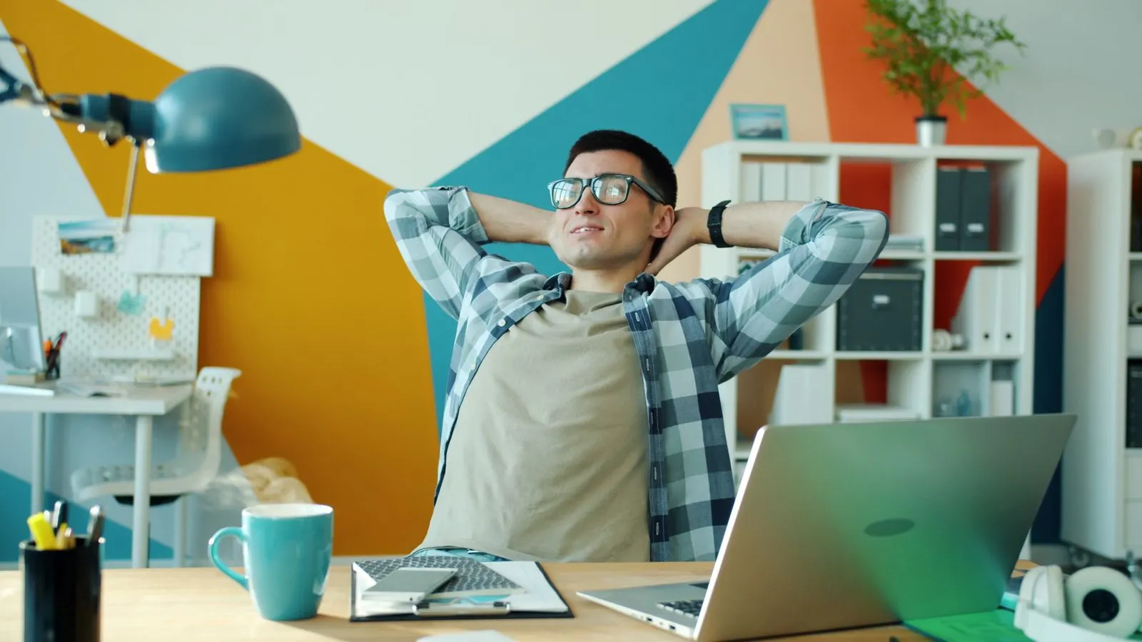 A man leans back in his office chair with his hands behind his head, relaxed at a tidy desk
