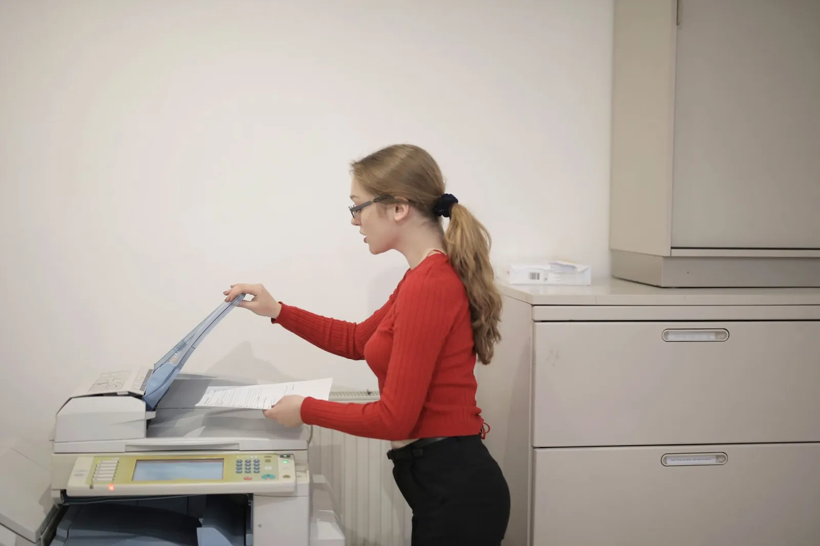 A woman in a red jumper lifts the lid of an office photocopier to scan a document