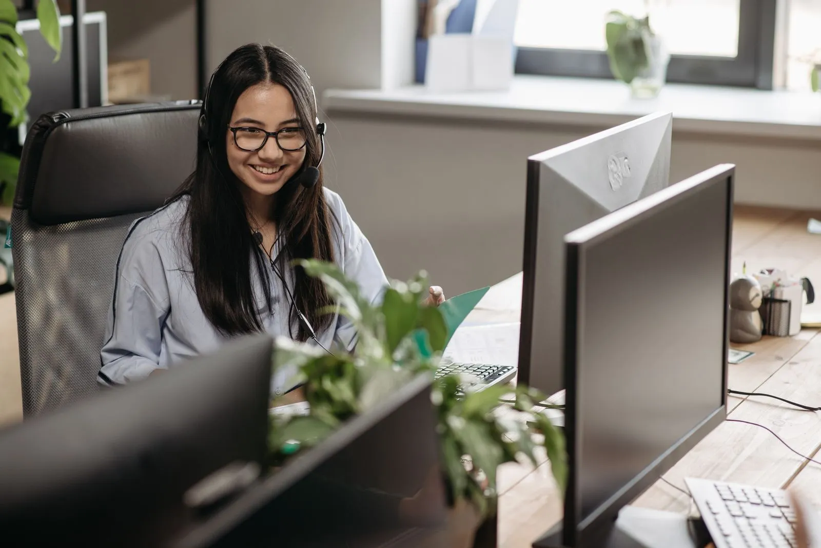 A smiling technician with glasses and a headset at a desk with two monitors, the first stop in service desk ticket triage