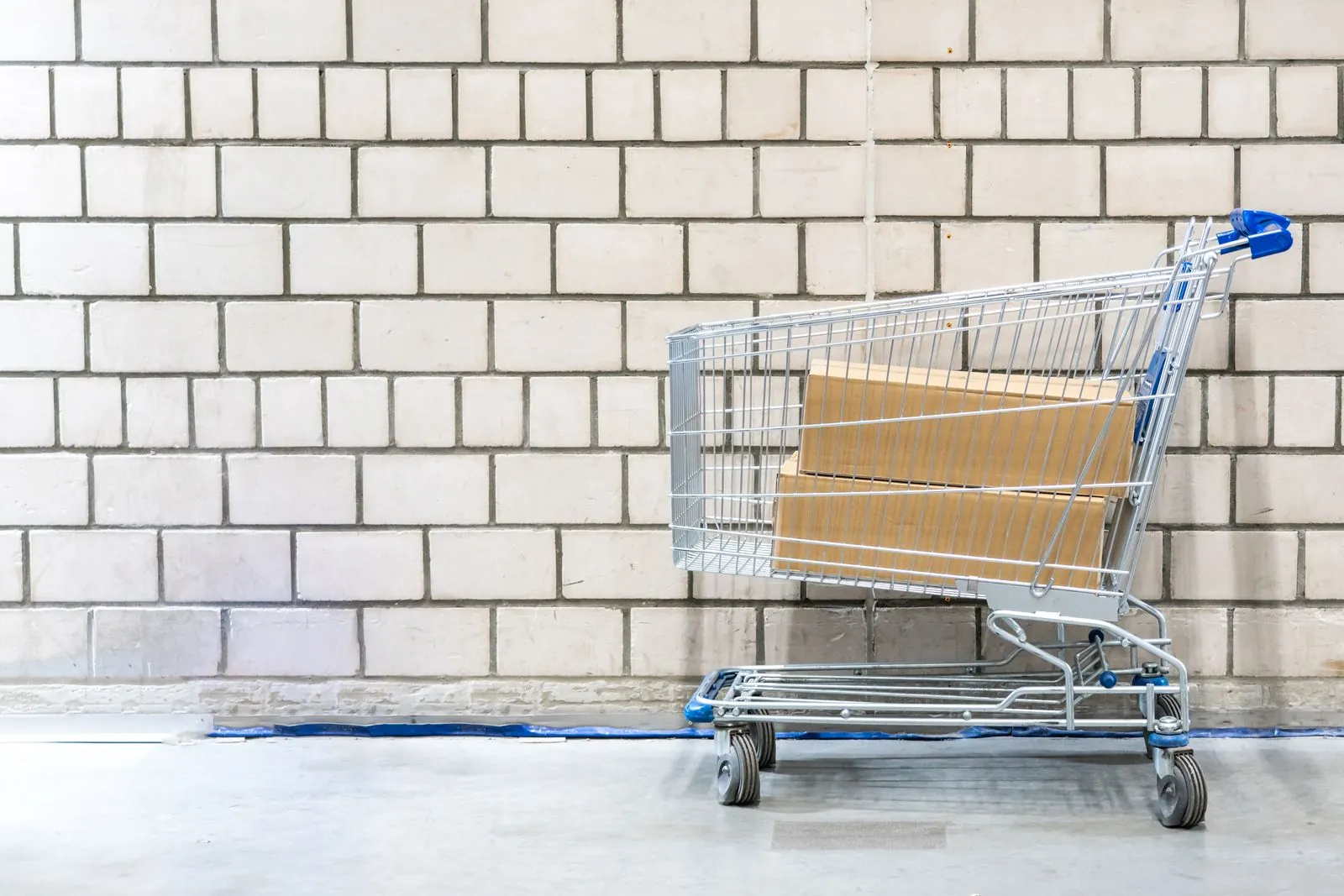 A shopping trolley holding two cardboard boxes against a pale concrete block wall