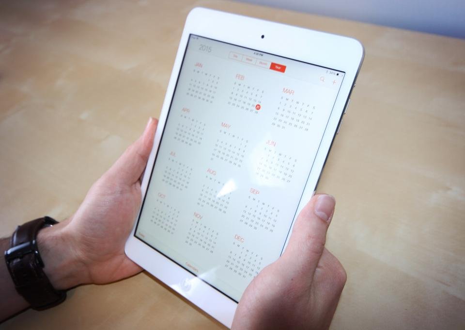 Hands holding a tablet showing a calendar, the kind of screen where a site diary can fill itself in from weather and sign-in data