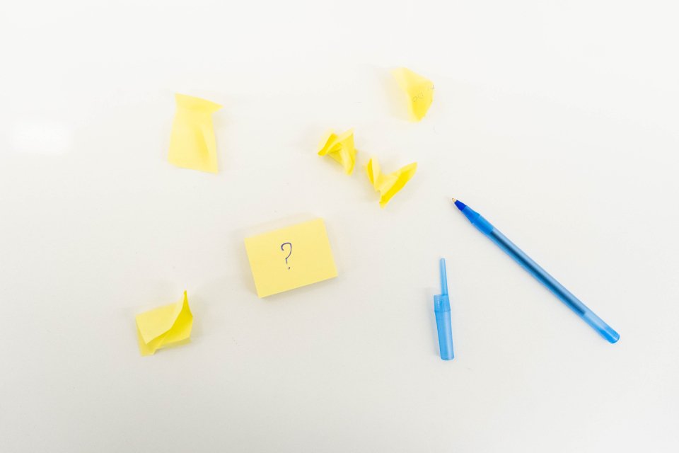 Crumpled yellow sticky notes and pens on a white desk, one note marked with a question mark