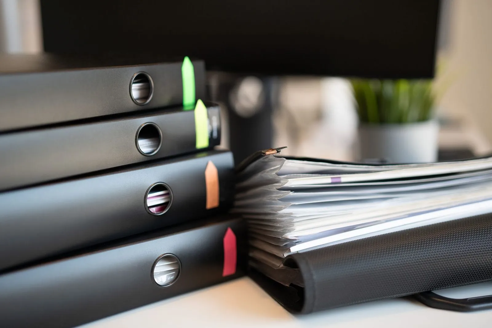 Black ring binders with coloured tab dividers stacked on a white office desk