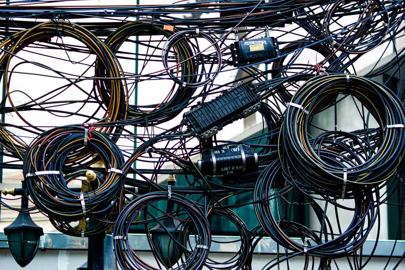 A dense tangle of black power and communication cables coiled around a utility pole with junction boxes