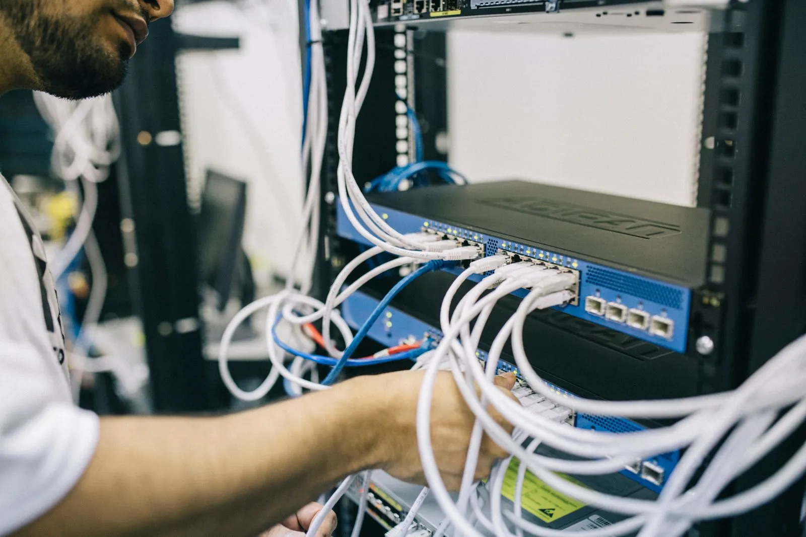 A technician's hand among white patch cables plugged into a blue network switch in a server rack