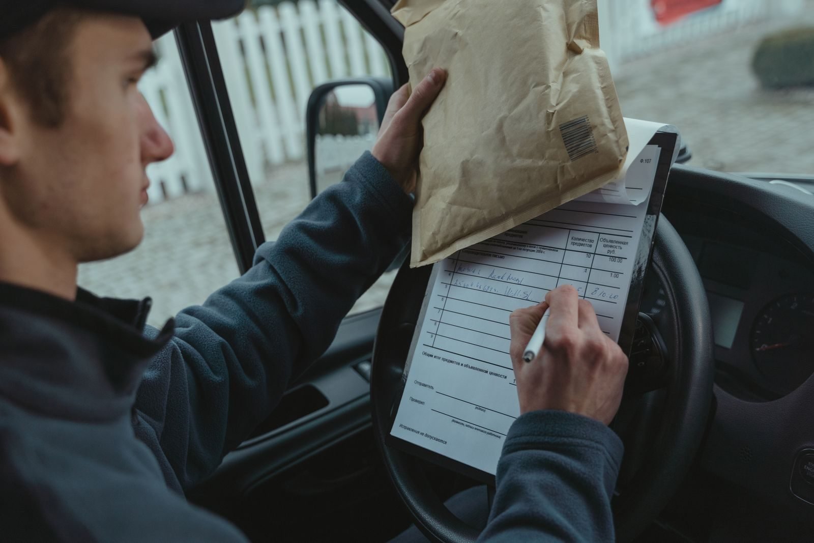 A delivery driver writing on paperwork resting on the steering wheel, the moment Waste Tracker records should be updated at pickup