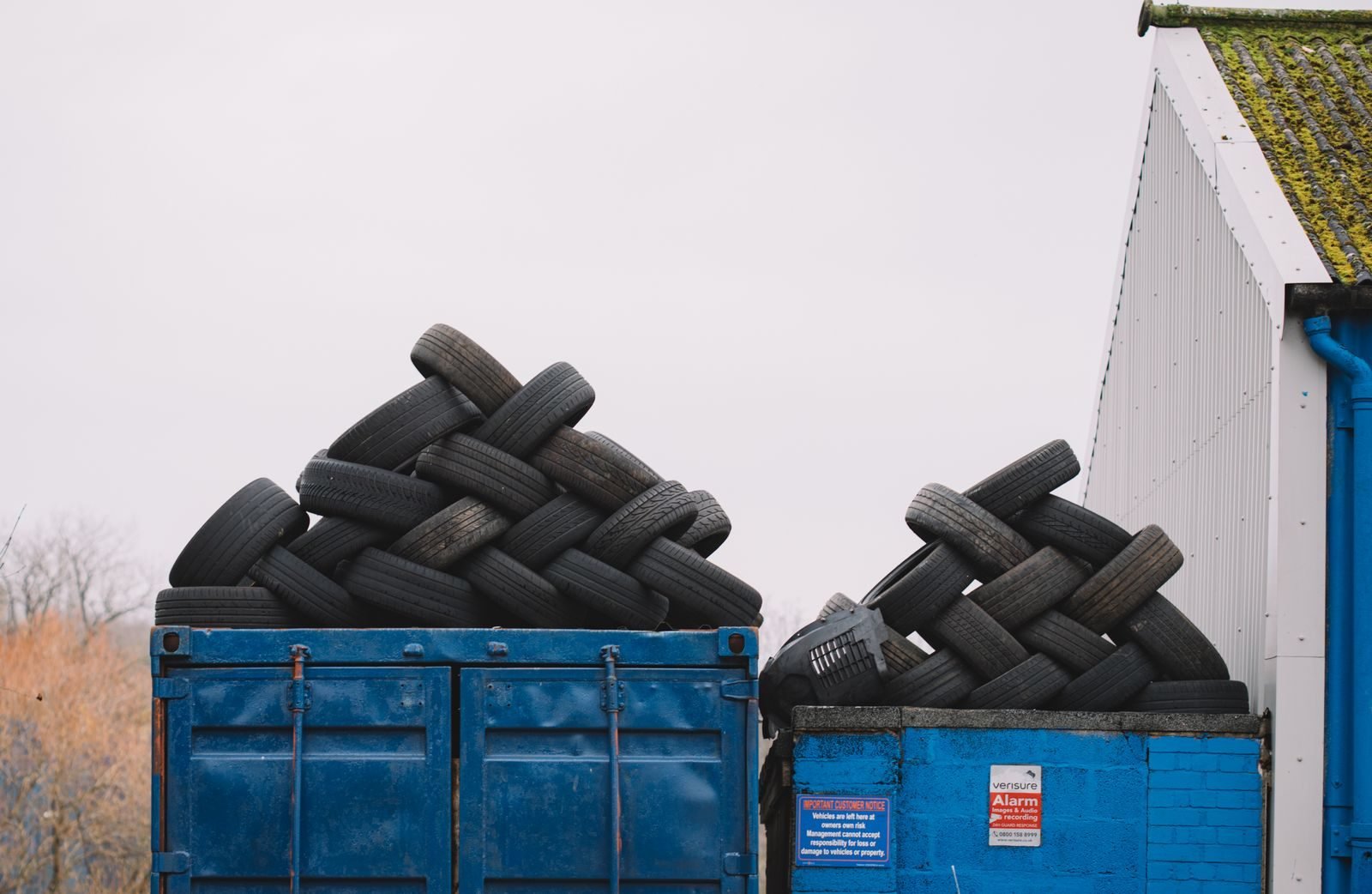 Used tyres piled high in two blue skip bins beside a shed, each load needing its own Waste Tracker record