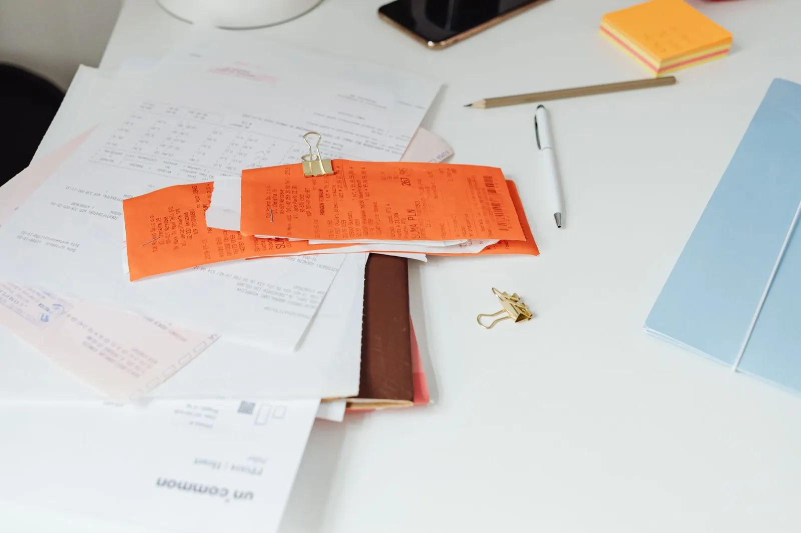 Orange and white paper receipts clipped together on an office desk next to a pen and folders